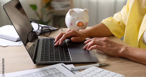 Person typing on laptop beside a piggy bank.